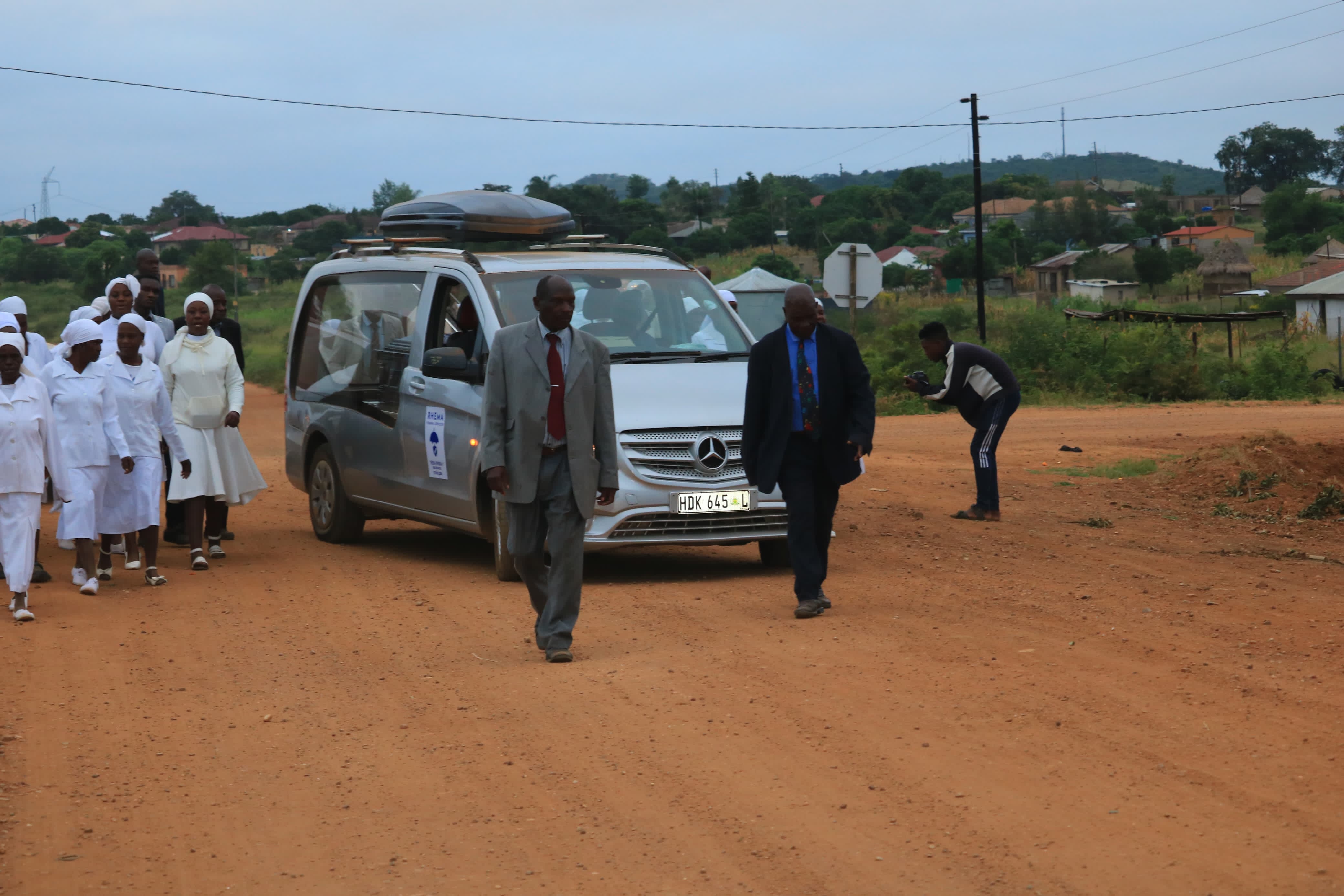 Funeral service vehicle and mourners gathered at venue